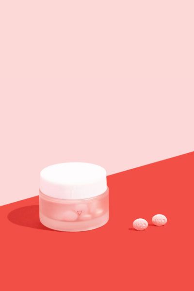 Wisp glass jar on pink and red surface with two pills outside the bottle