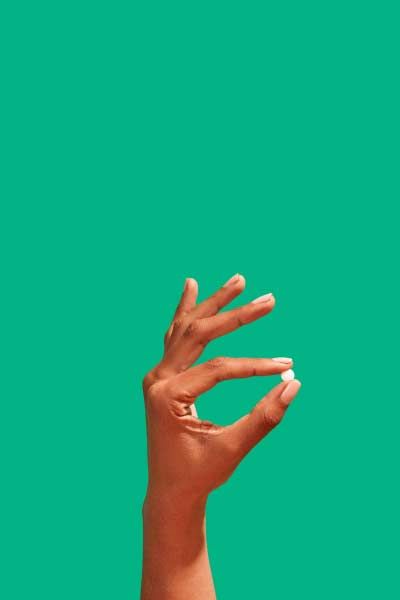 A woman's hand holding an emergency contraception pill in front of a green background