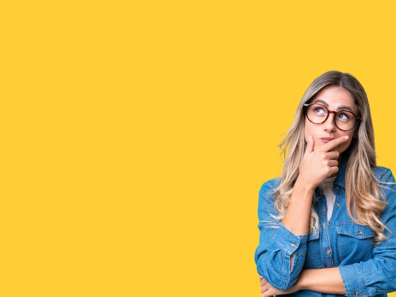 A woman with blonde hair and wearing a denim shirt and looking confused with a yellow background