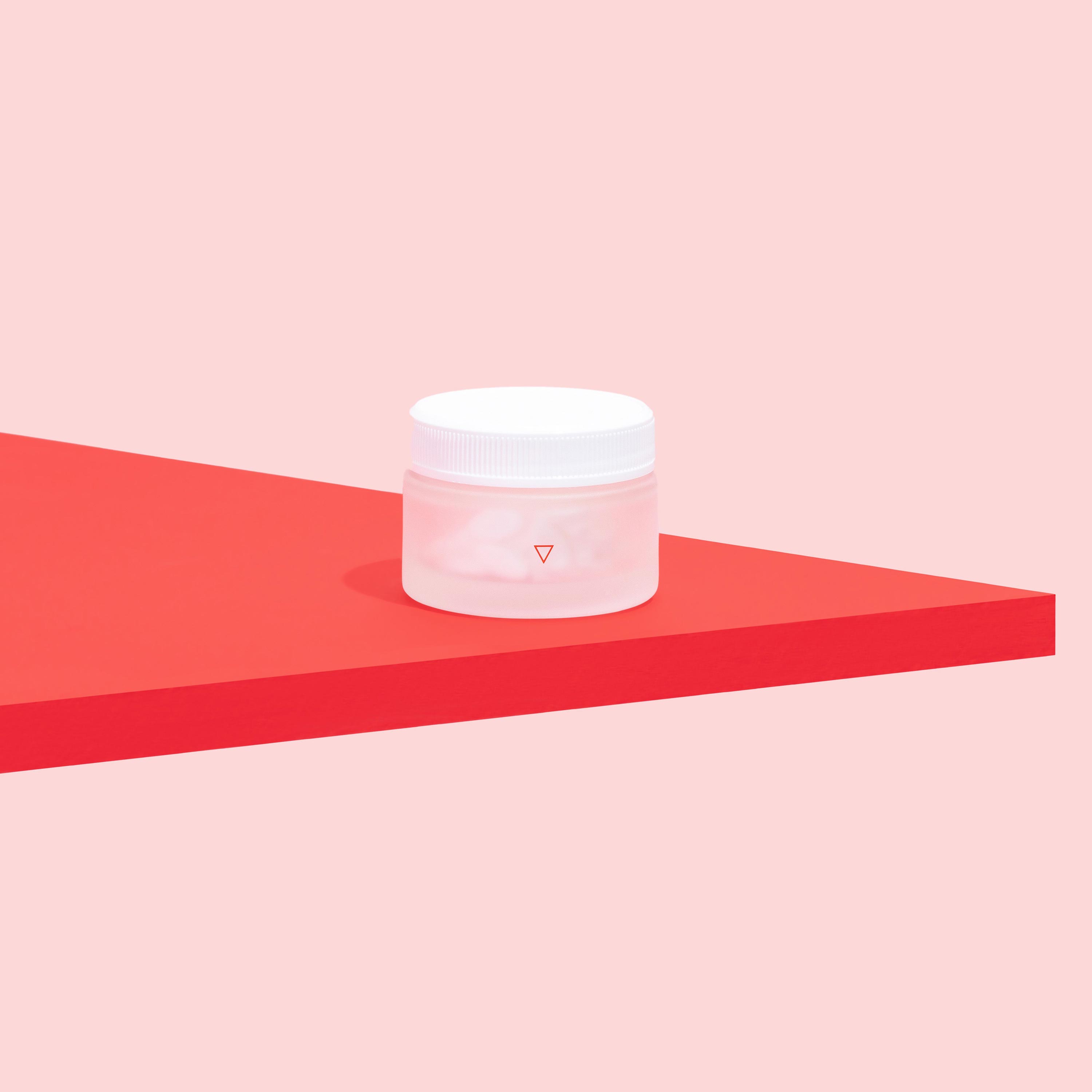 Jar of Norethindrone Acetate to delay your period on a pink background and red surface