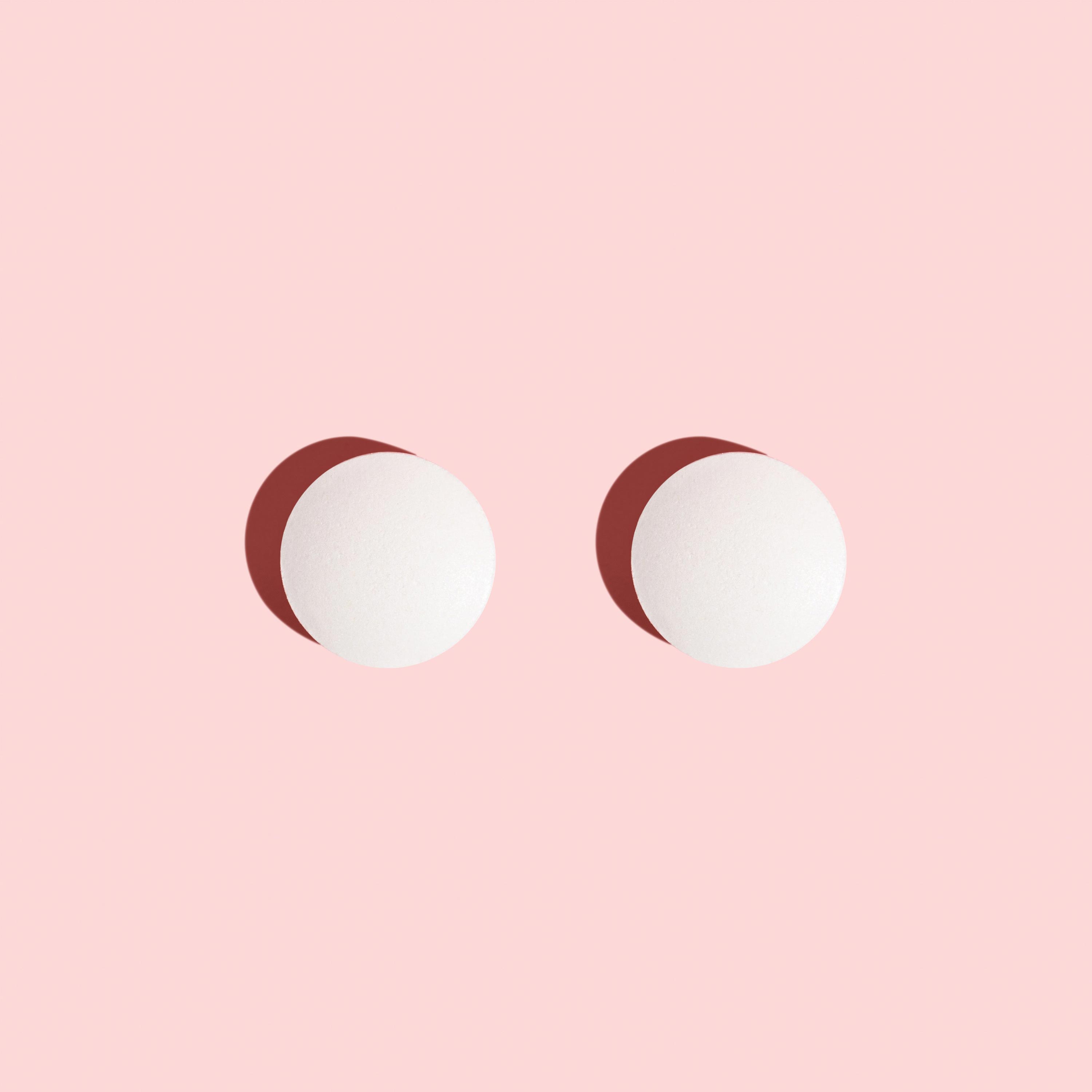 Two probiotic pills for women's health on a pink background