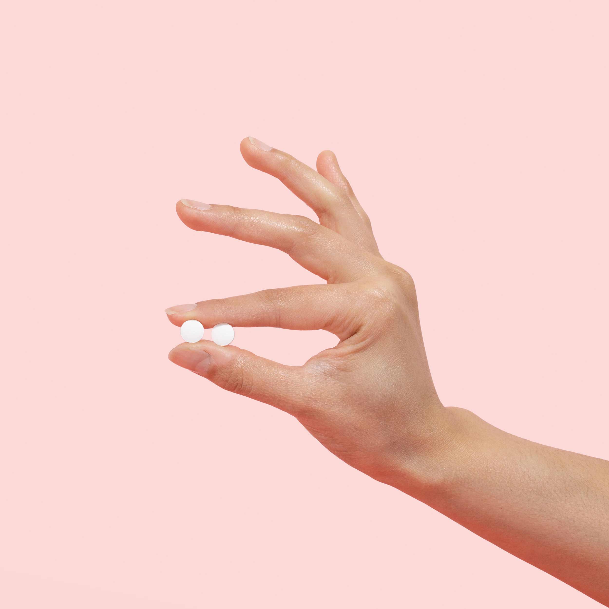 Woman's hand holds two probiotic pills against a pink background