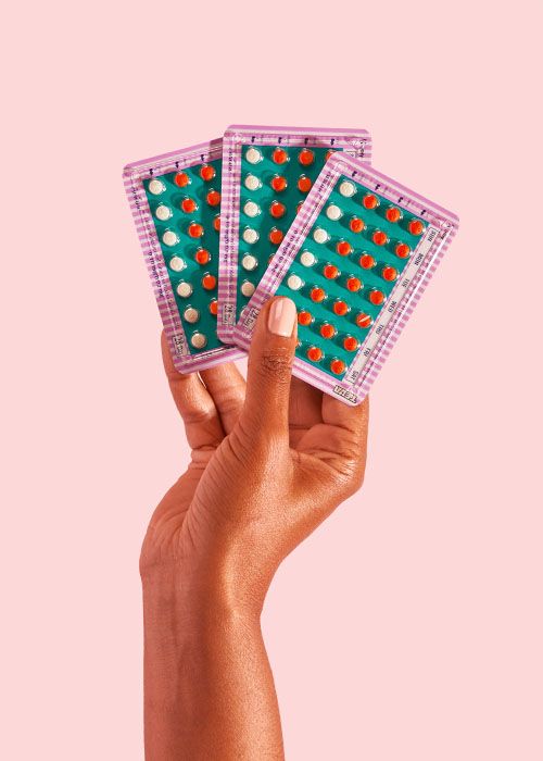 woman's hand holding colorful birth control packets on pink background