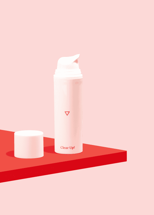 Bottle of Wisp Clear Up! Acne Cream sitting on a red surface on a pink background