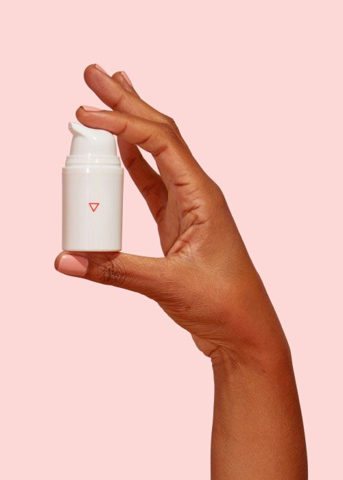 Hand holding bottle of Wisp Estradiol Cream on a pink background