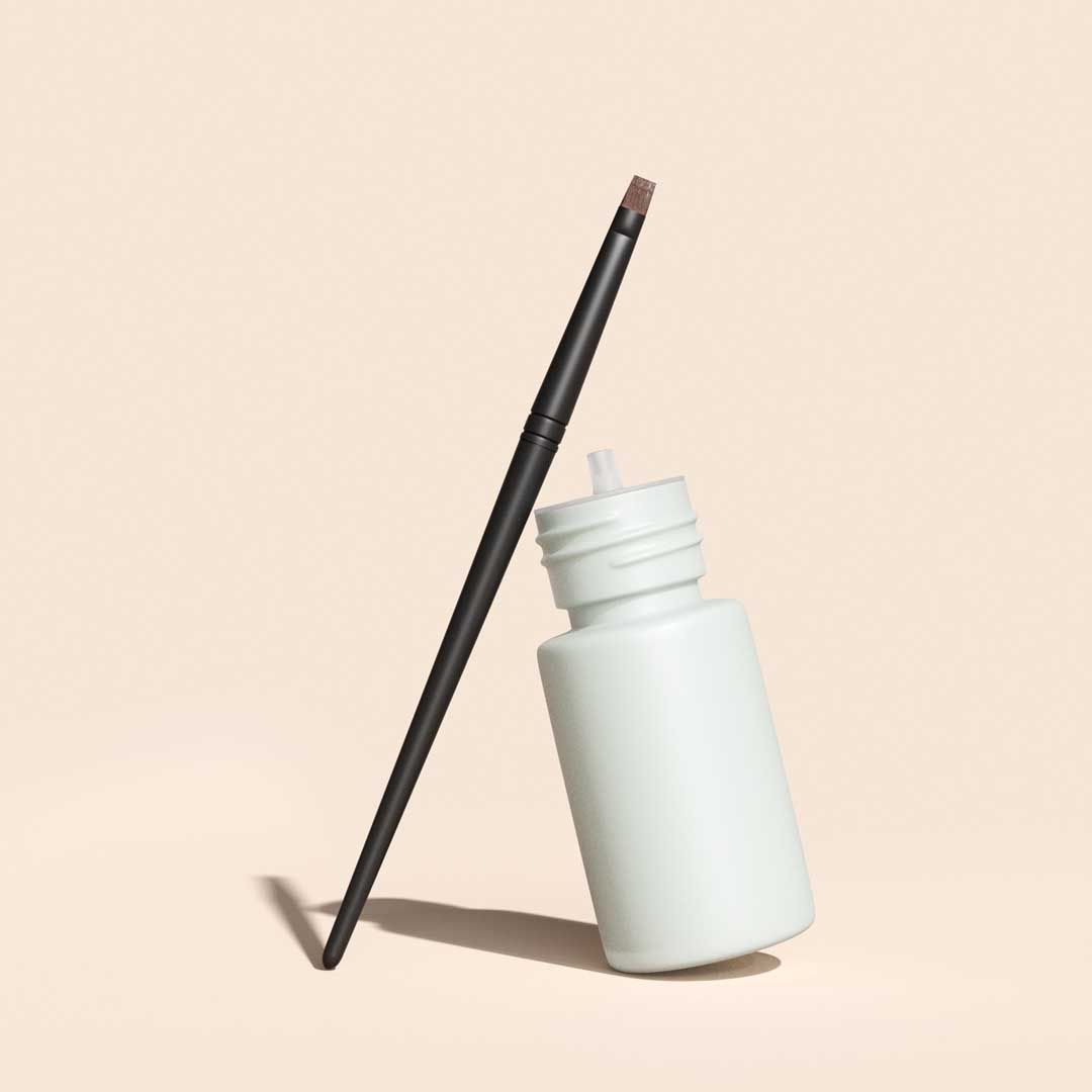 A bottle of Bimatoprost and applicator brush on a cream surface