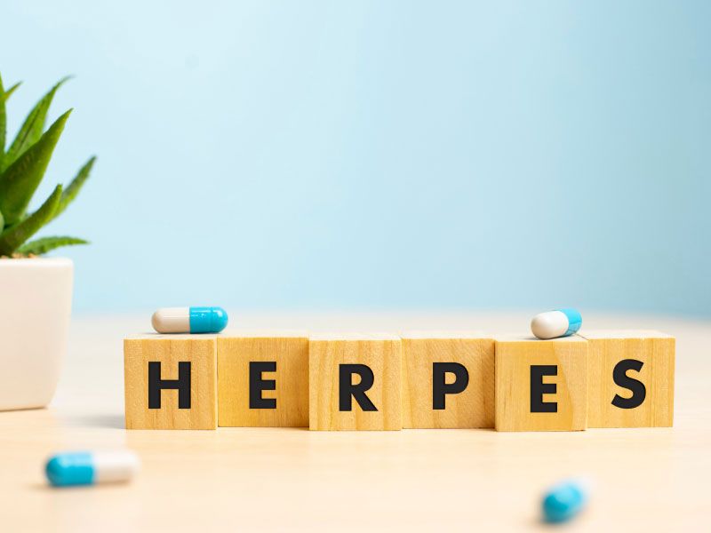 The word Herpes spelled out on wooden blocks with blue and white pills, a plant and a blue background