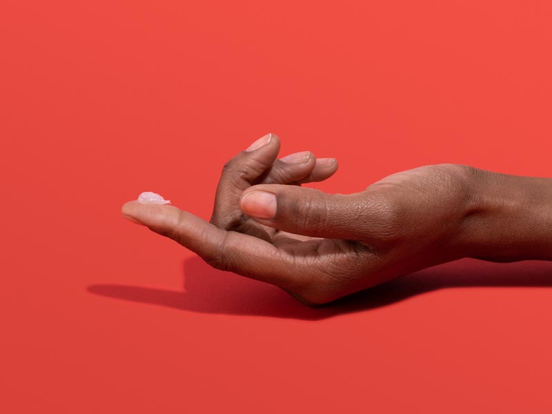 A woman's hand with Acyclovir Cream on the index finger and a red background