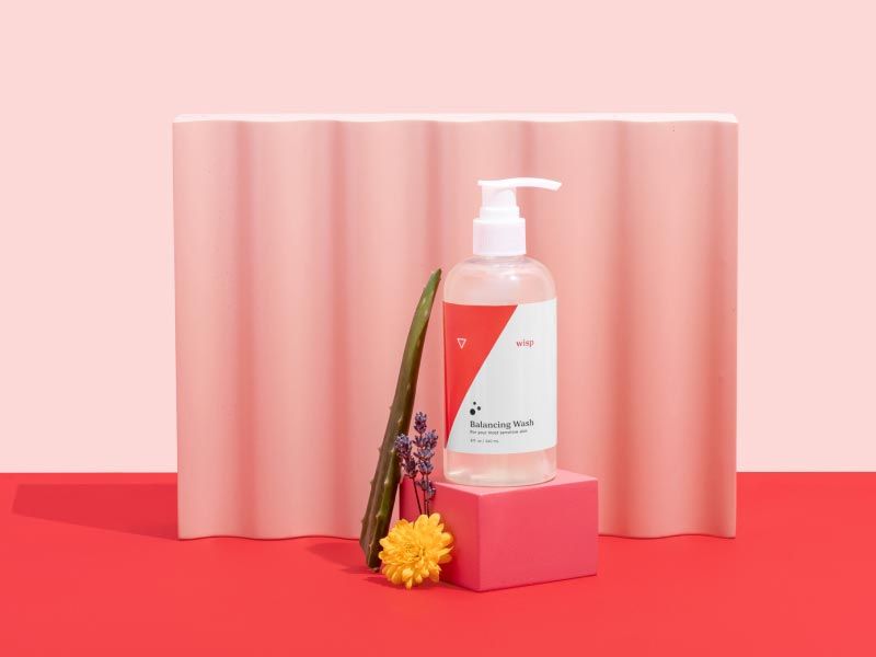 Wisp Balancing Wash with Aloe Vera, Lavender, Marigold and colorful abstract shapes on a pink and red background