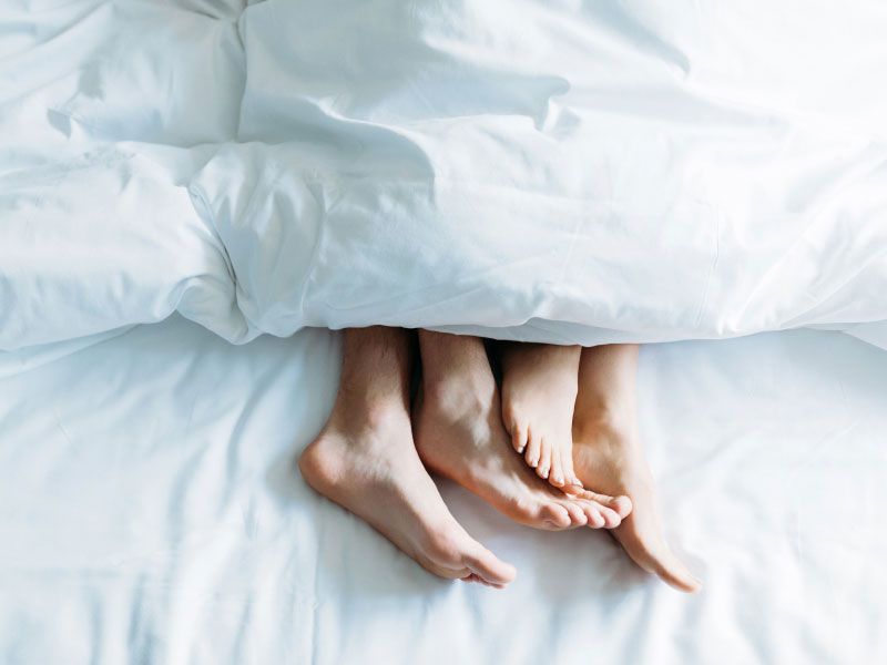 A couple's feet sticking out from underneath a white comforter