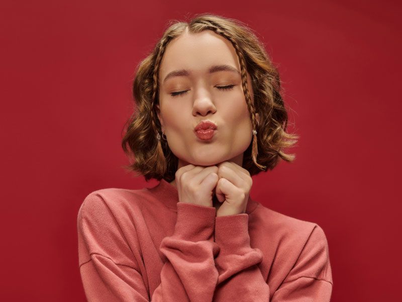 Woman wearing a pink sweater pucker her lips with a dark red background