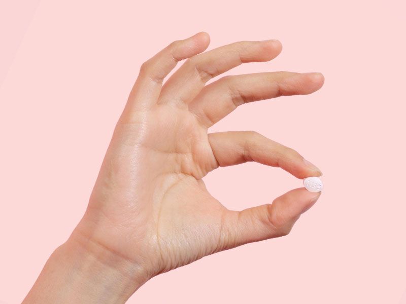 Hand holding a single Fluconazole pill with a pink background