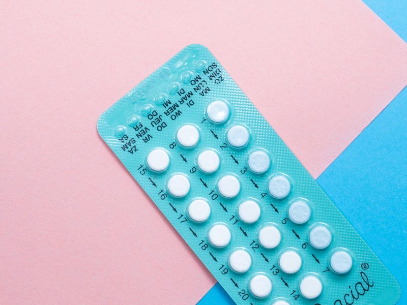A blue birth control packet on a pink and light blue background