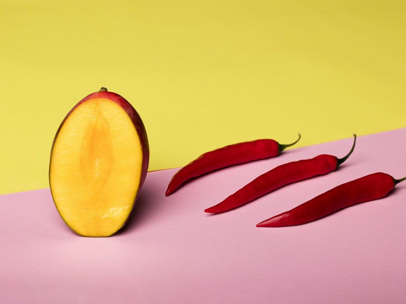 Cut open fruit and red peppers on a yellow and pink background
