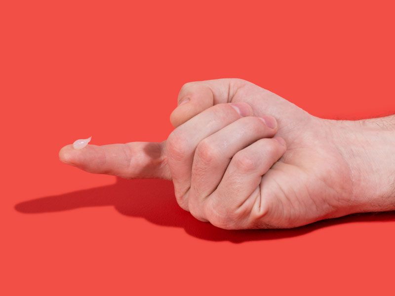 Man's hand with Acyclovir cream on his index finger with a red background
