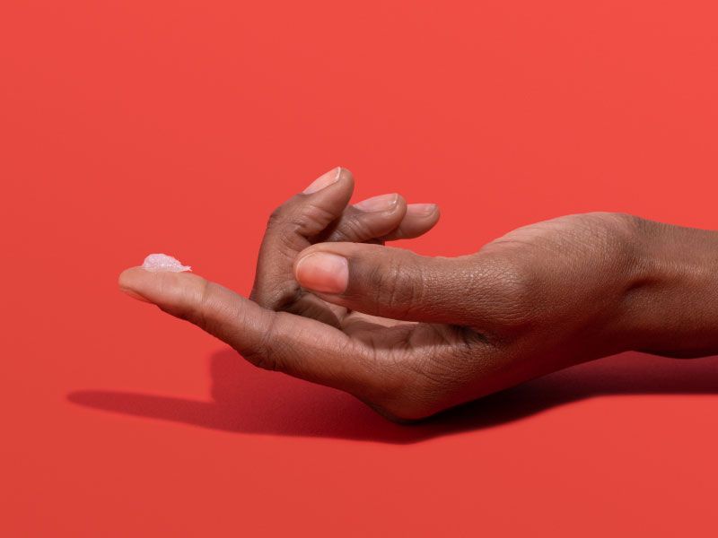 Woman's hand with Acyclovir cream on her fingertip with a red background