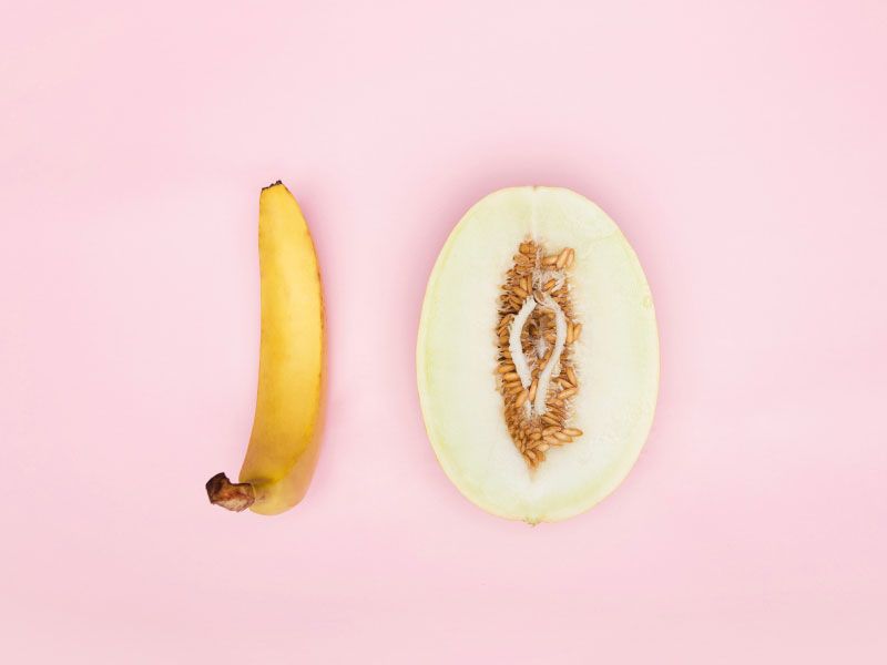 A suggestive cut open fruit and a banana on a pink background
