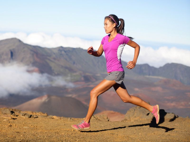 a woman in a pink shirt trail running under blue skies with mountains in the background