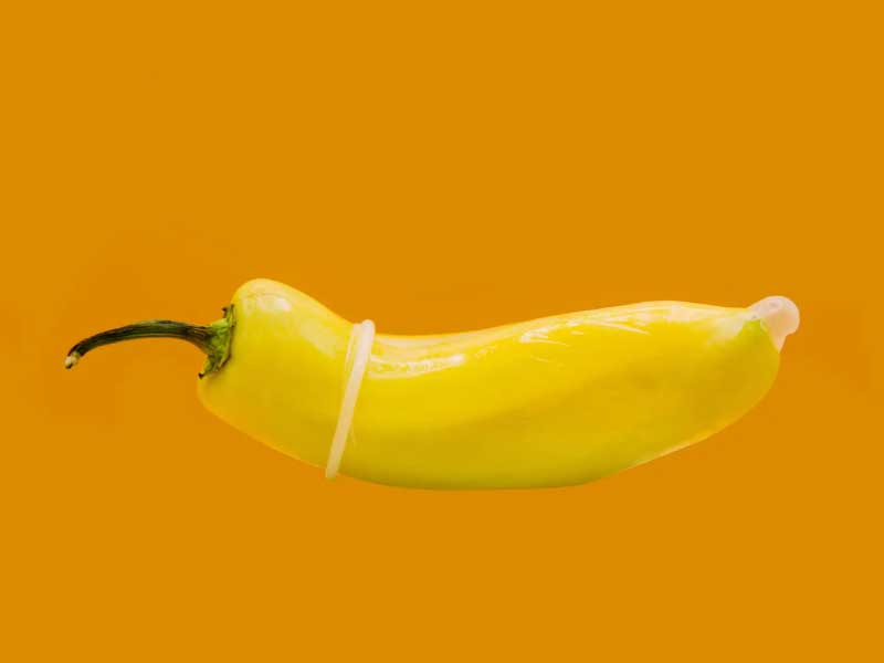 A yellow pepper with a condom on it in front of an orange background