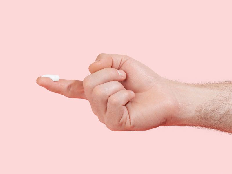 Man's hand with lidocaine cream on the index fingertip with a pink background