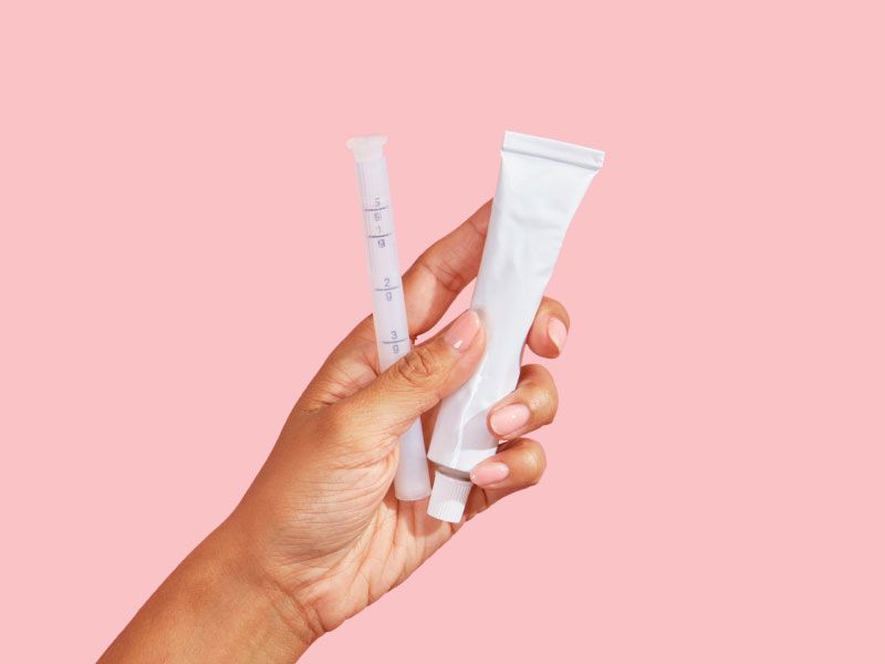 Female hand holding a tube of vaginal dryness cream and applicator with a pink background