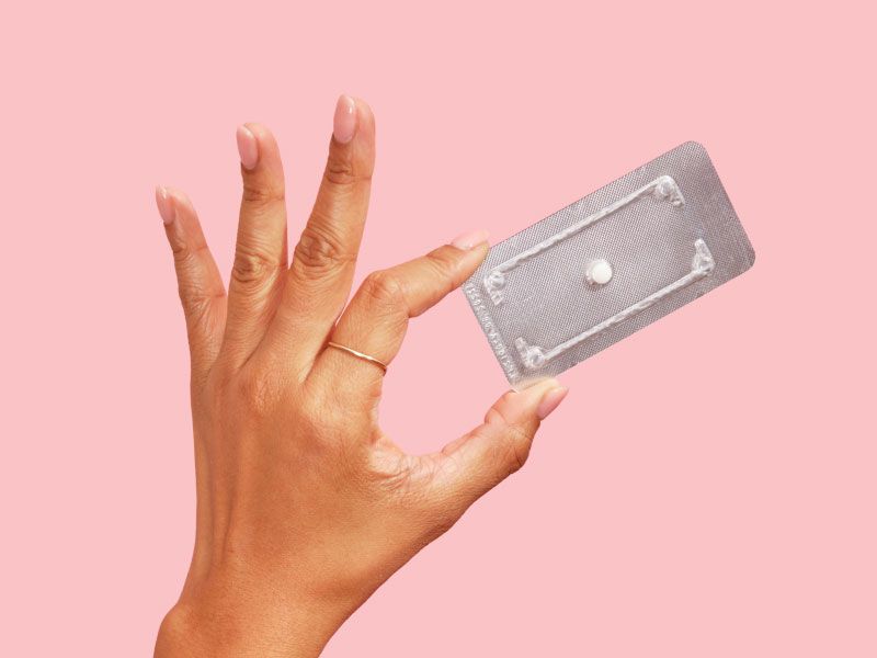 Woman's hand holding a Plan B packet with a pink background
