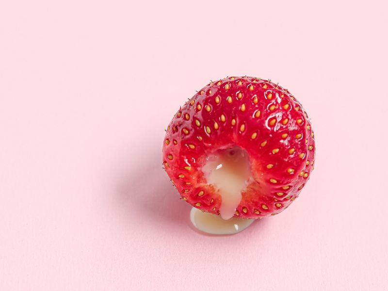 a raspberry oozing a creamy filling on a pink background