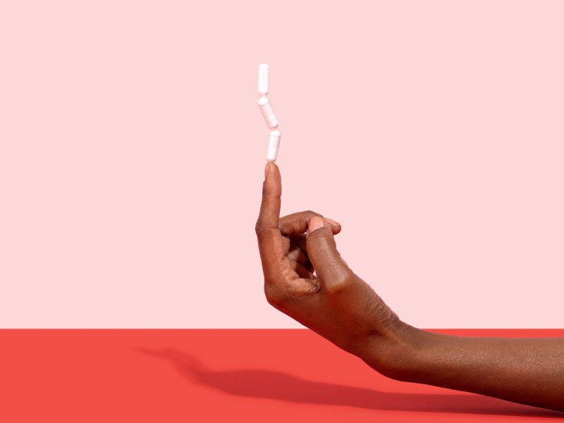 Hand balancing 3 pills on their pointer finger with a pink and red background
