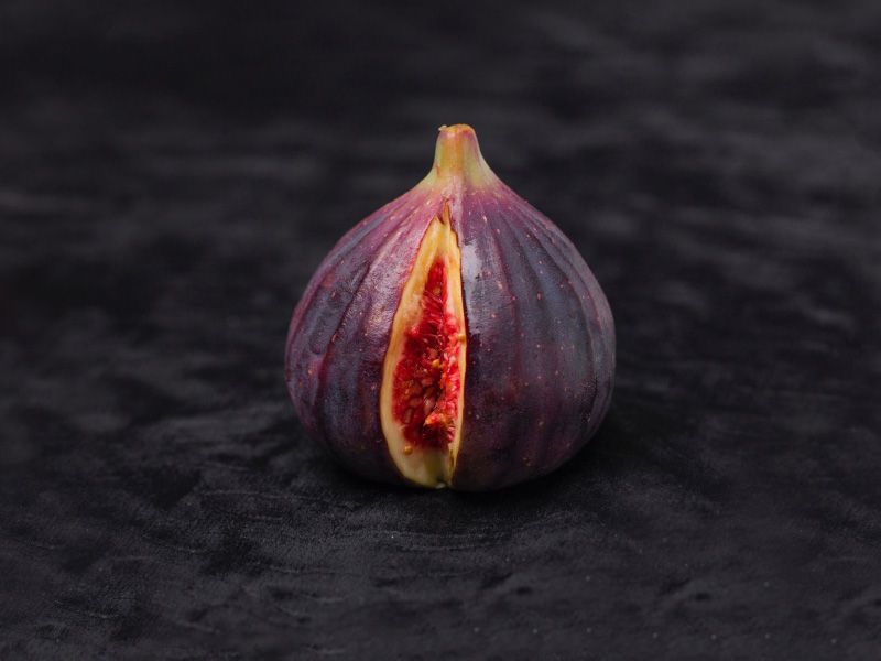 a fig sliced open to resemble a vulva on a dark background