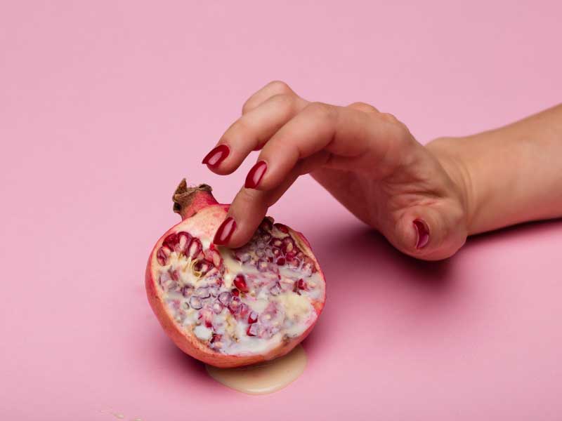 A woman's hand is seductively touching an cut open fruit on a pink surface