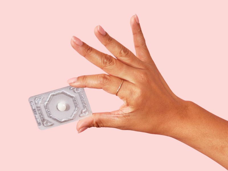 a woman's hand holding emergency contraception on a pink background