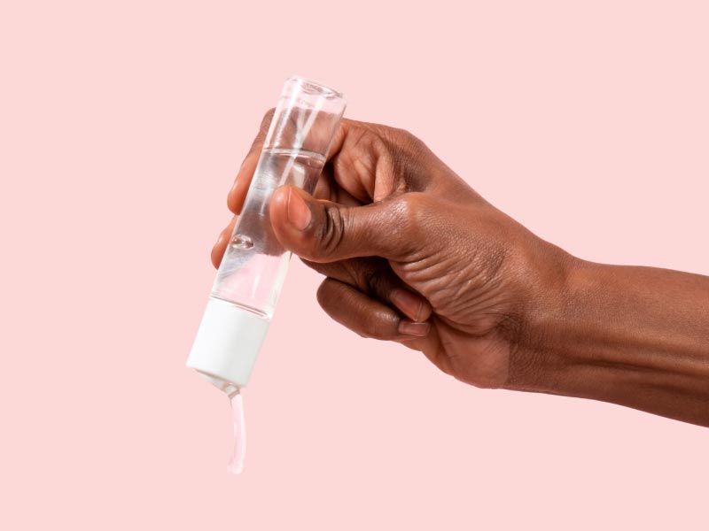 A woman's hand holding Wisp Harmonizing Lube over a pink background