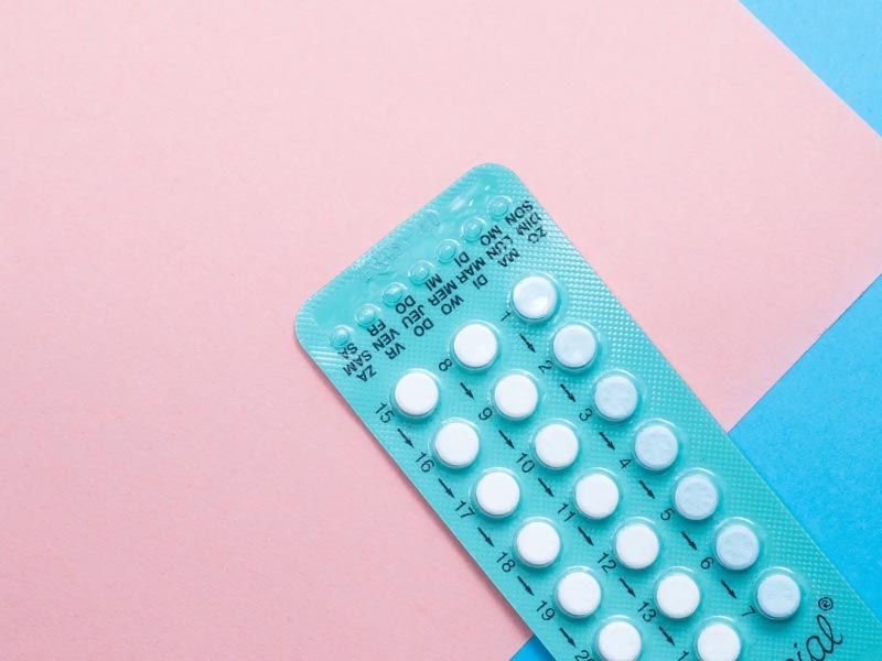 A blue birth control packet on a pink and light blue surface