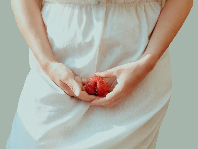 A woman wearing a tan dress holding a strawberry in her hands