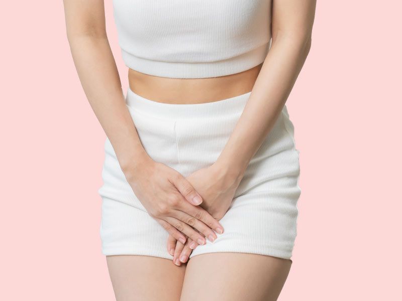 Woman with her hands over her pelvic region indicating discomfort with a pink background