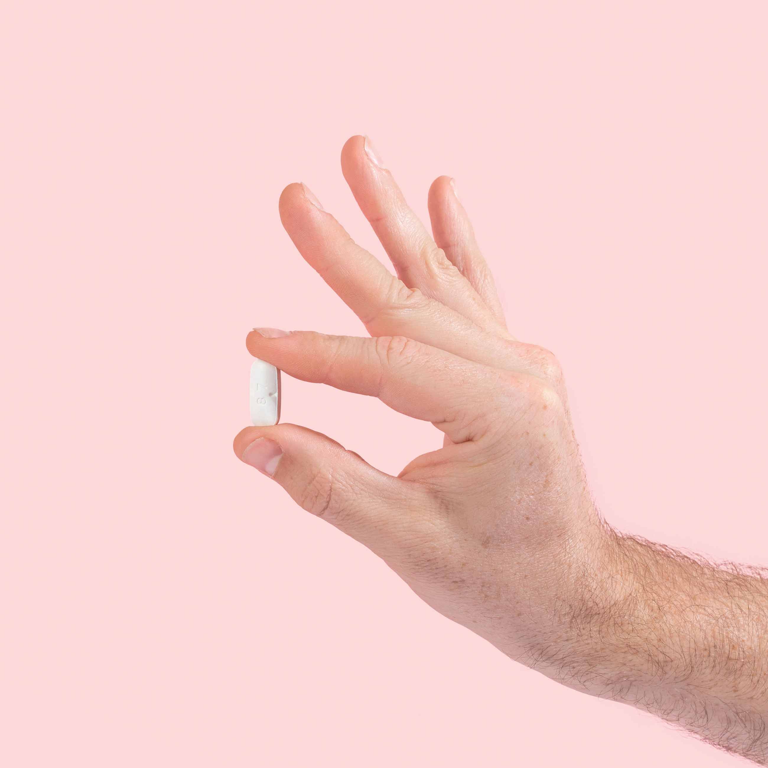Male hand holding valacyclovir tablet on a pink background