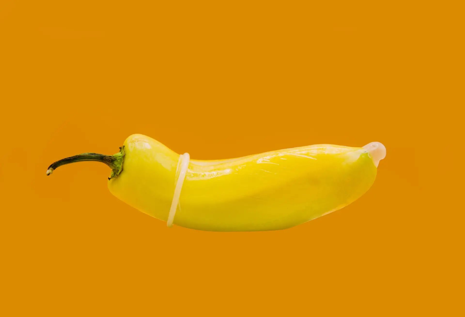 A yellow pepper wrapped in a condom on an orange background