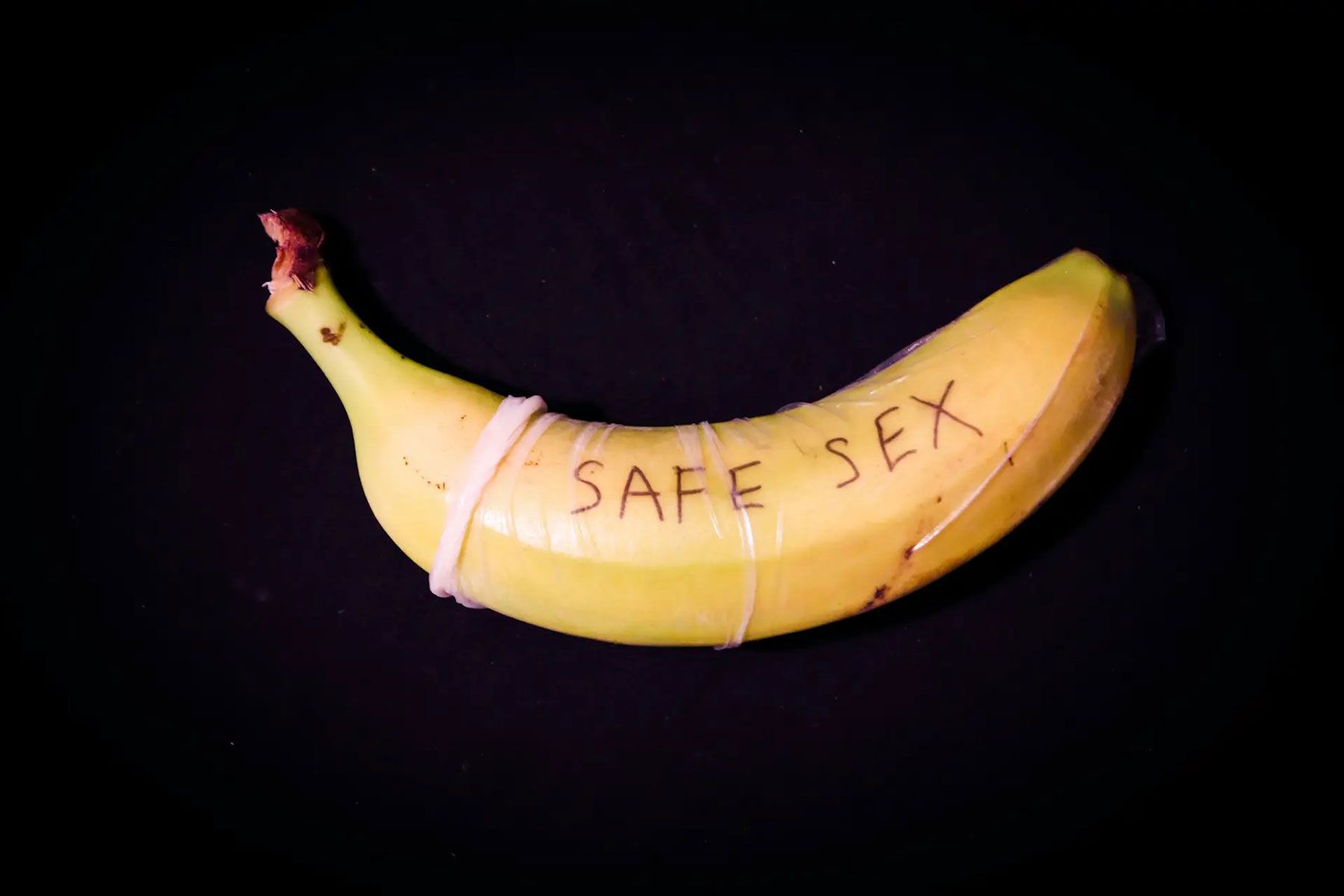 banana wrapped in a condom with the words "safe sex" written on it on a black background