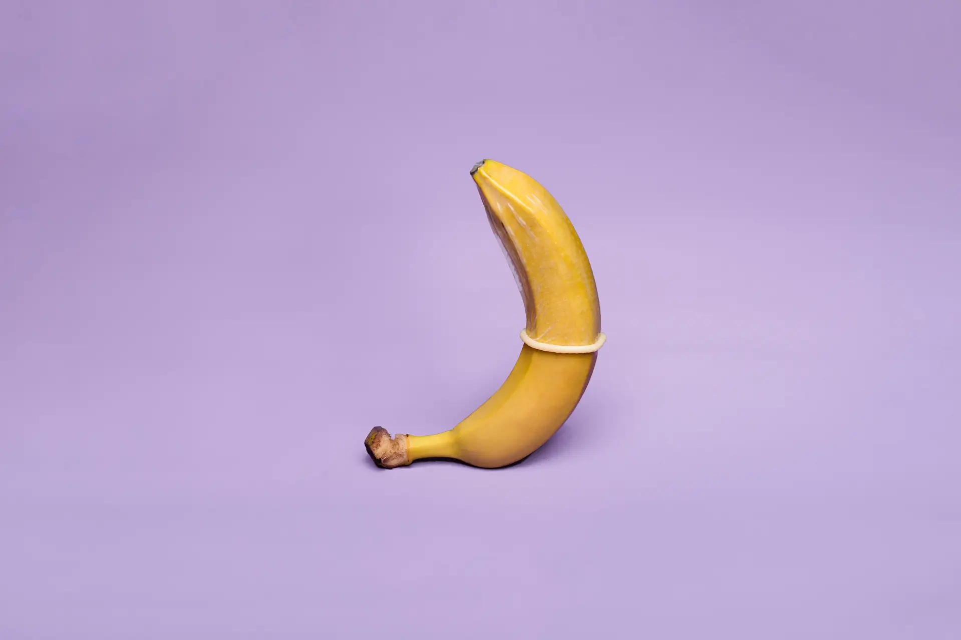 a banana with a condom on it on a purple background