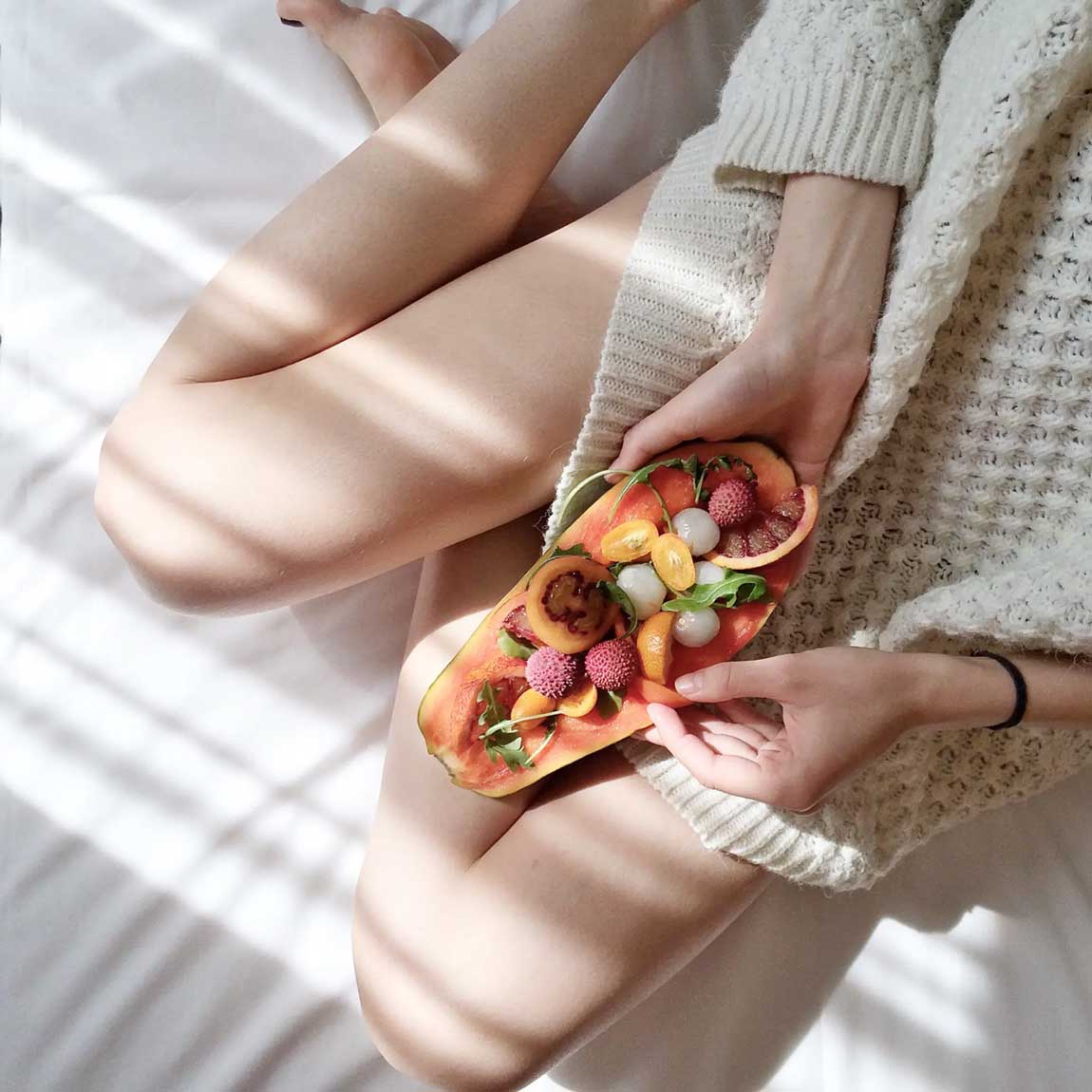 a woman eating a fruit platter in bed