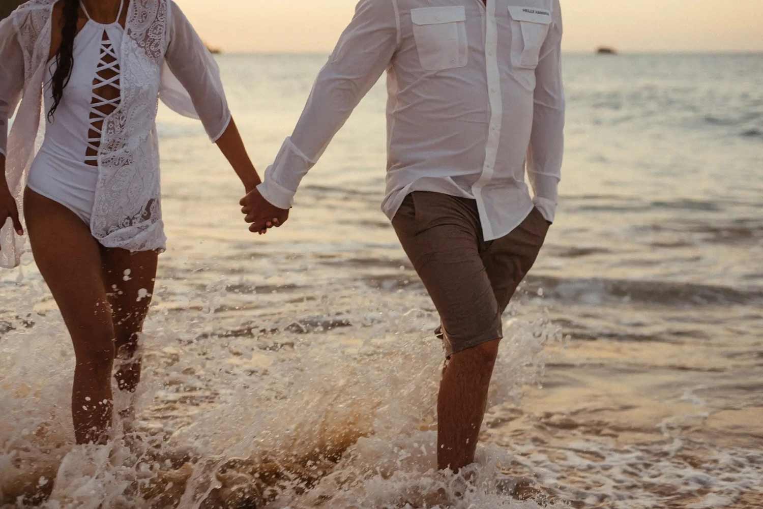 A man and woman holding hands while walking through water at the beach