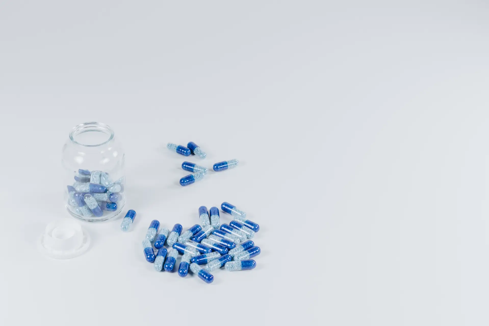 Pills in a glass jar and scattered on a white surface