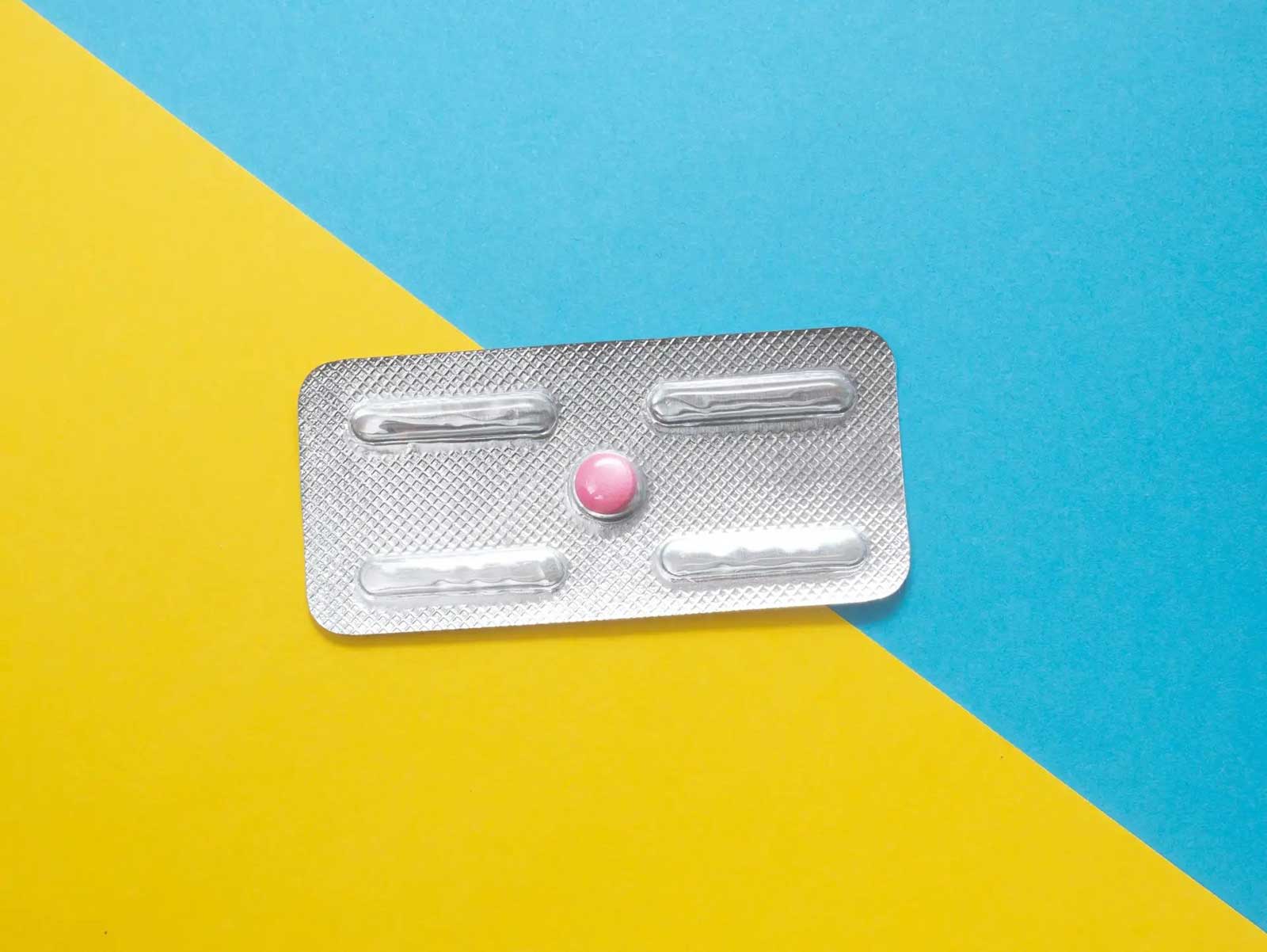 An emergency contraception pill in a foil packet on a blue and yellow background