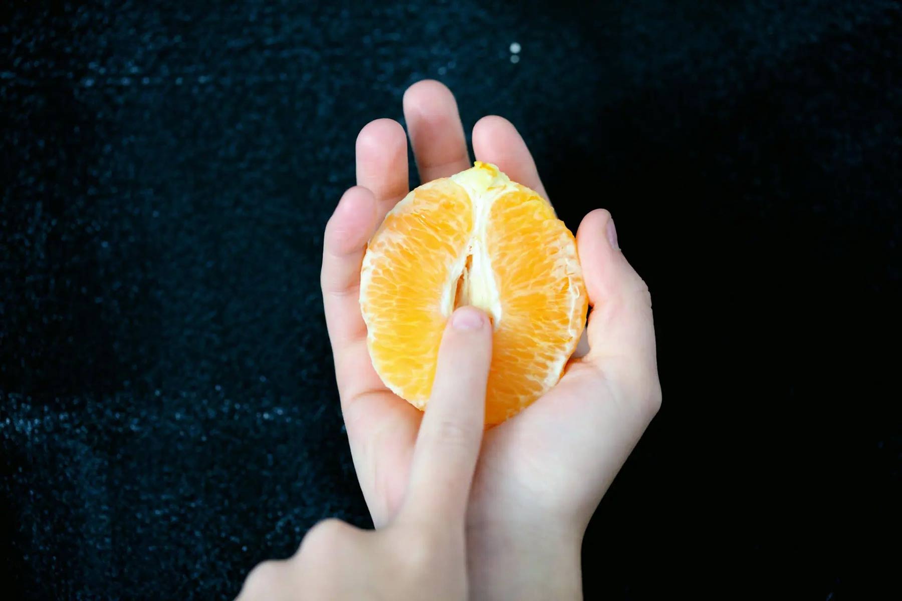 a woman's hands holding half an orange while suggestively touching the center
