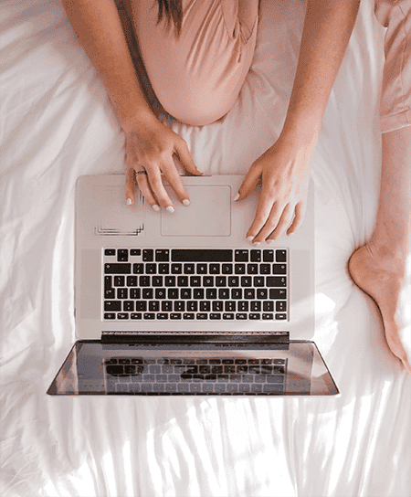 Woman's hands typing on a laptop in bed