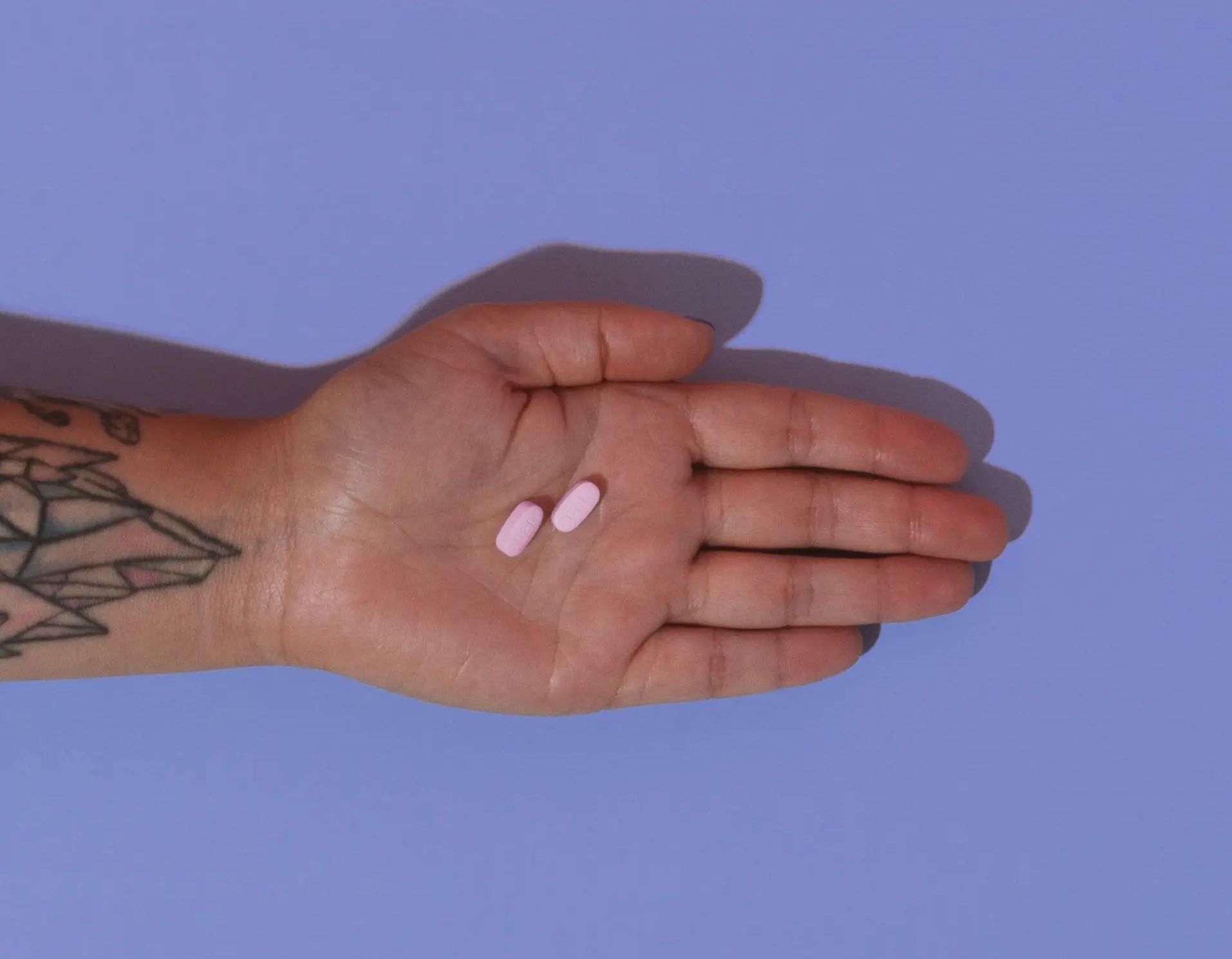 a hand holding two pink pills on a purple background
