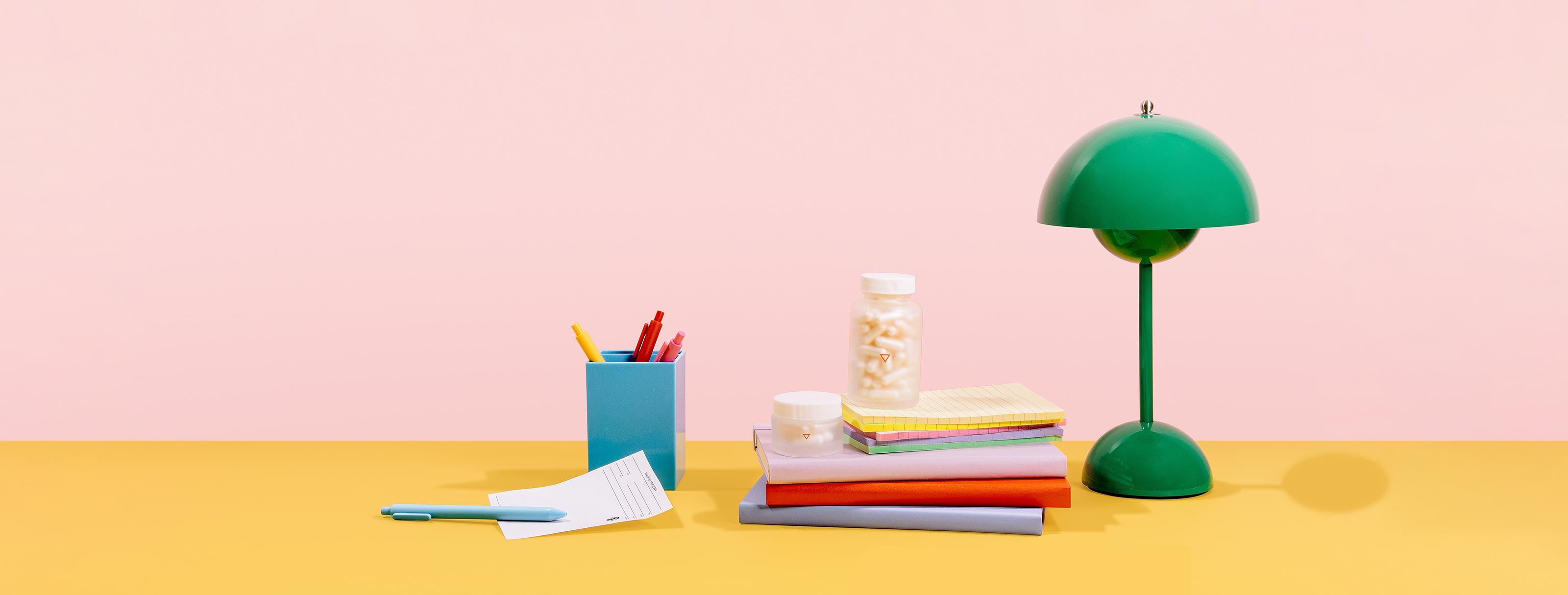 Medications in discreet packaging sit on yellow desk surface against a pink wall