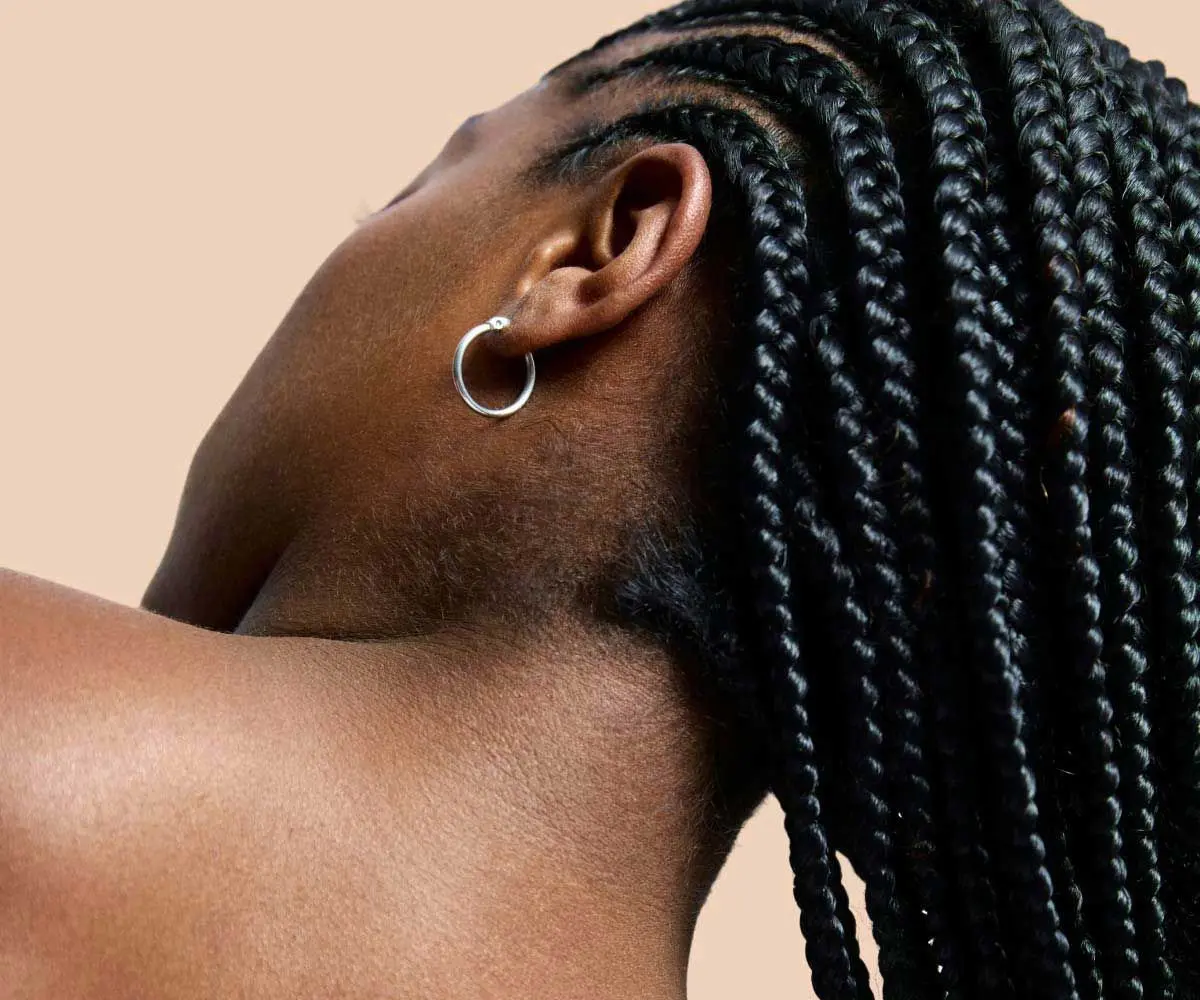 A close up of a woman's neck and shoulders with clear skin in front of a cream background