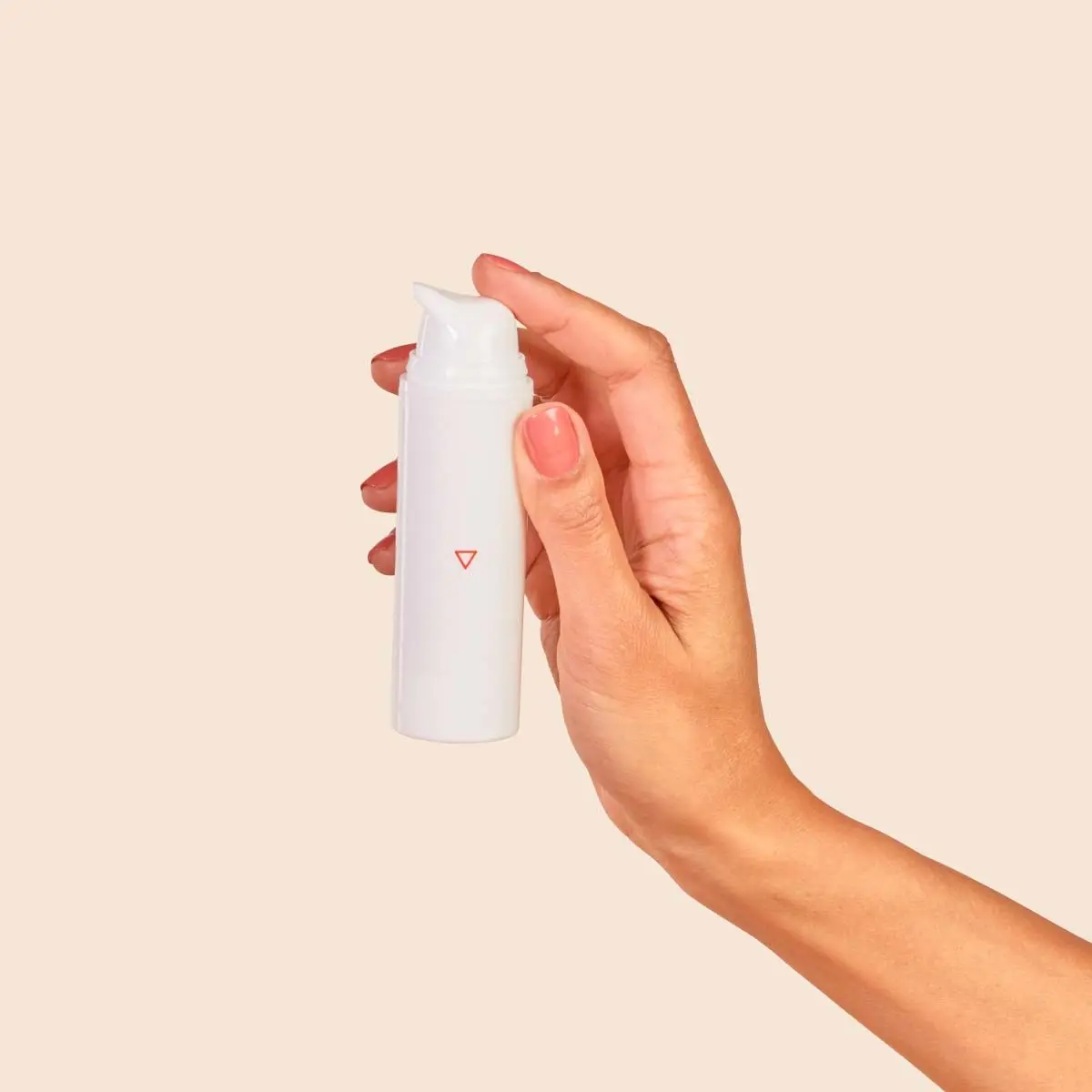 A person's hand holding a pump bottle with a cream background