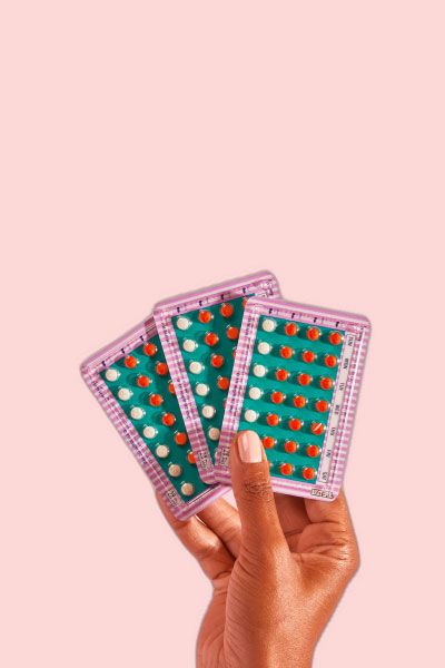 Hand holding 3 packets of birth control on a pink background